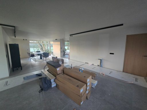 Unmöblierter Raum mit Kartons und Bauarbeiten, große Fenster im Hintergrund.