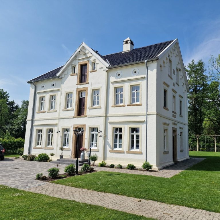 Aufnahme einer von uns gestrichenen Fassade einer Villa. Sie befindet sich freistehend im grünen und ist in weiß bzw. hellen Beigetönen gestrichen.