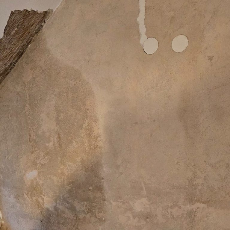 Wasserschadenbeseitigung Eine Wand mit verletztem Putz, sichtbaren Wasserflecken.